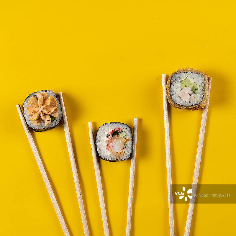 上图是用筷子夹住黄色背景的寿司图片素材
