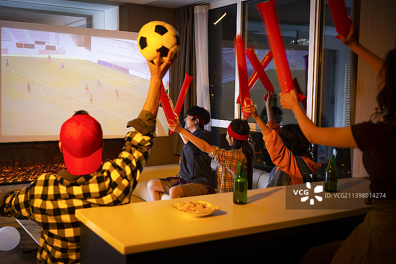 快乐的年轻人在客厅观看足球比赛:欢呼呐喊庆祝胜利图片素材