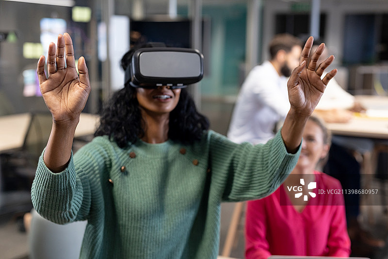 微笑的年轻非洲裔美国女商人穿着虚拟现实模拟器在办公室的手势图片素材