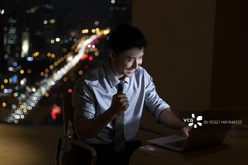 夜晚商务男子在酒店房间使用笔记本电脑加班工作，庆祝成功欢呼图片素材