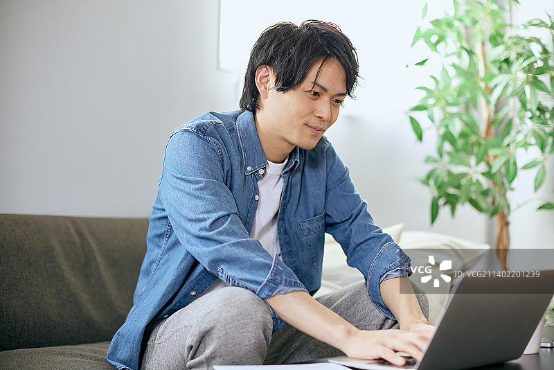 日本男子在沙发上使用笔记本电脑图片素材