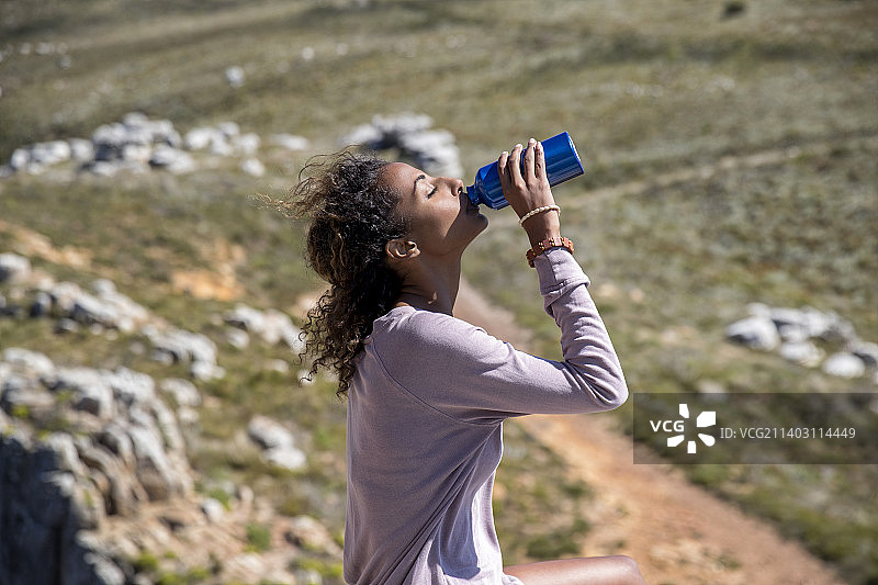 年轻女子在山里徒步旅行时用瓶子喝水图片素材