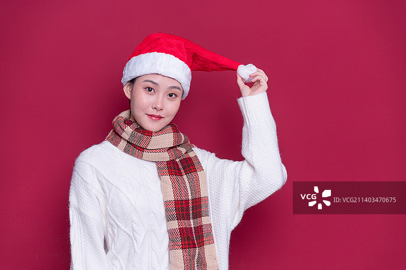 红色背景前带着圣诞帽的年轻女性图片素材