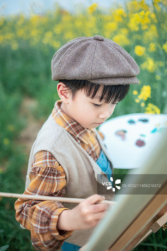 春天的油菜花田里一个小男孩在画画图片素材