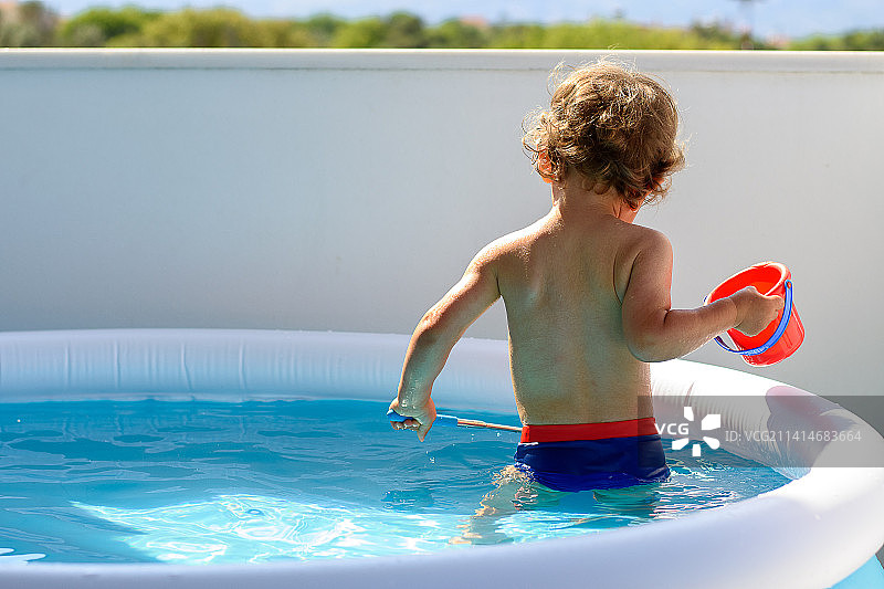 一个小男孩在阳台池水里用网钓鱼的背影图片素材