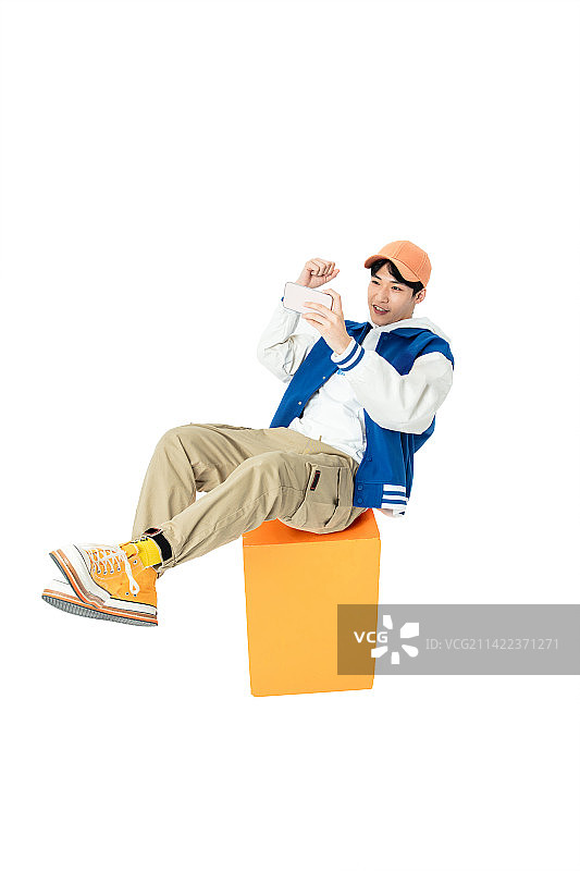 坐在橙色凳木箱子上玩手机的年轻男生图片素材