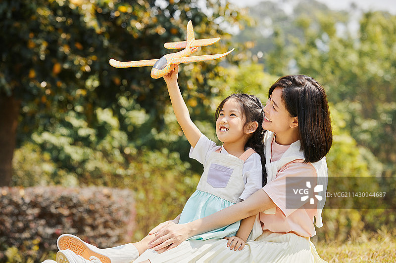 手拿飞机模型的小女孩坐在妈妈的腿上图片素材