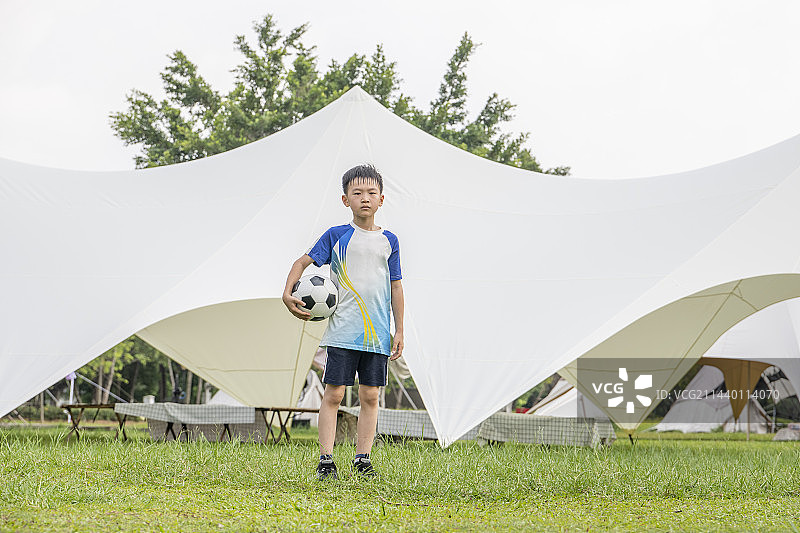 公园露营帐篷前抱着足球的小男孩图片素材