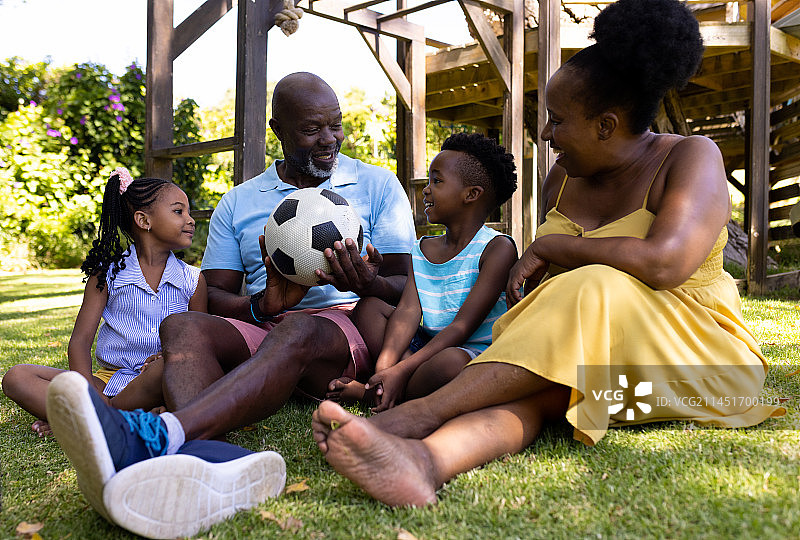 非洲裔美国人的祖父母和孙子坐在公园的草地上踢足球图片素材