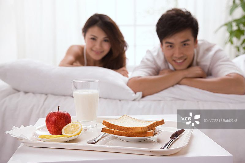 东方年轻夫妇趴在床上吃早饭图片素材