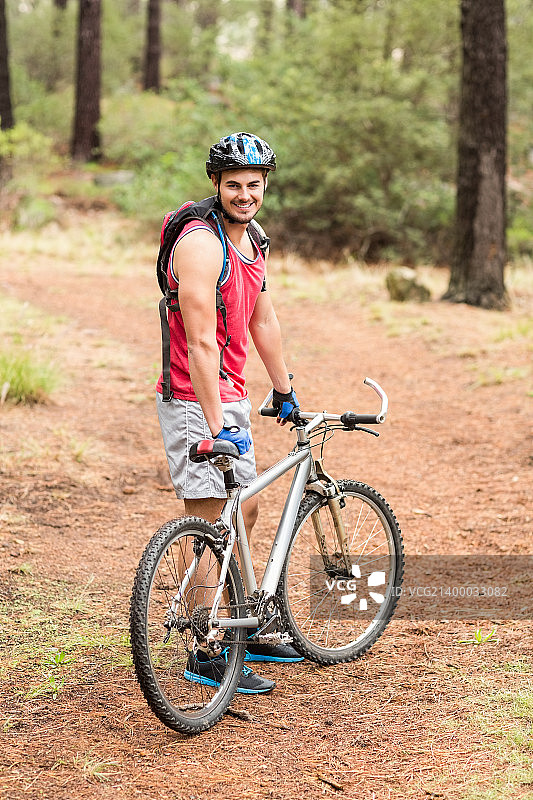 快乐英俊的摩托车手拿着自行车，在大自然中看着相机图片素材