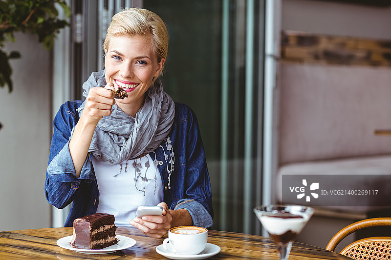 微笑的金发女郎在咖啡厅享受一块巧克力蛋糕图片素材