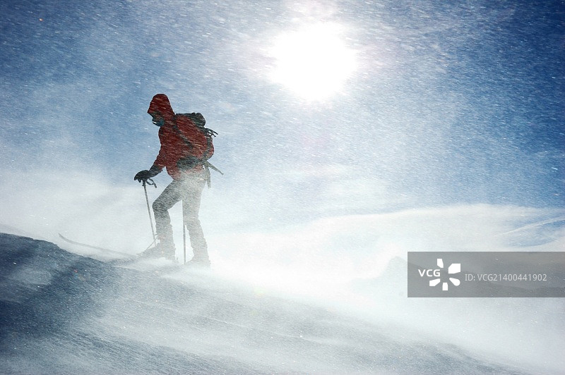 一个在暴风雪中到达山顶的孤独的野外滑雪者，水平方向图片素材