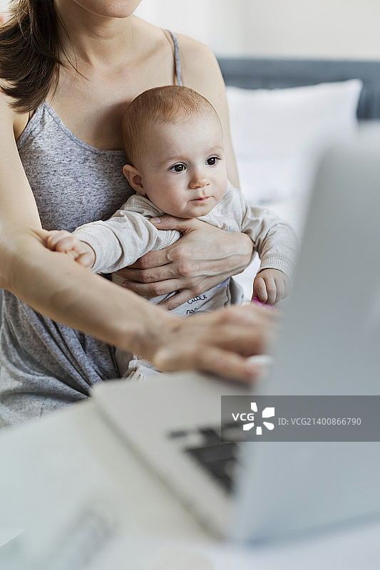 妈妈抱着宝贝女儿，在笔记本电脑前工作图片素材
