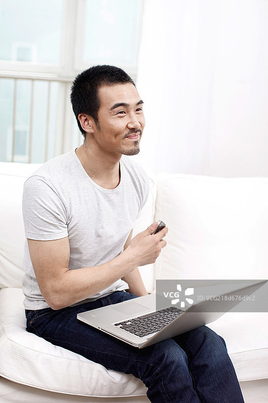 一个坐在白色沙发上用笔记本电脑的青年男士图片素材