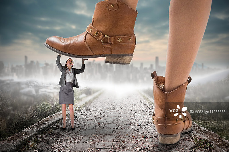 牛仔靴踩在女商人身上的合成图像，通向地平线上的大城市图片素材