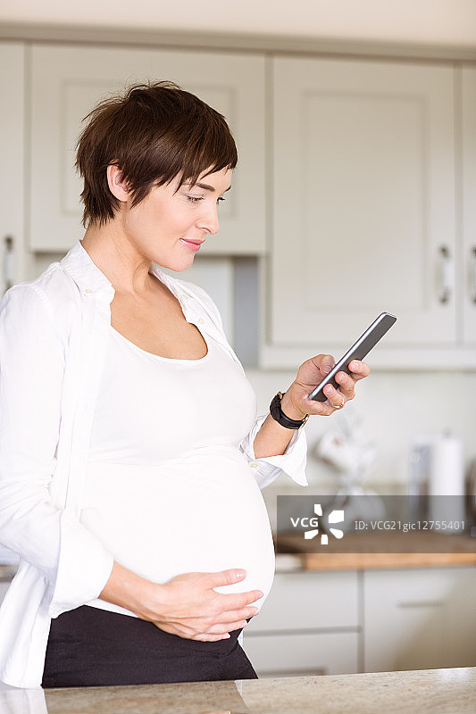 一名孕妇在厨房里使用智能手机图片素材
