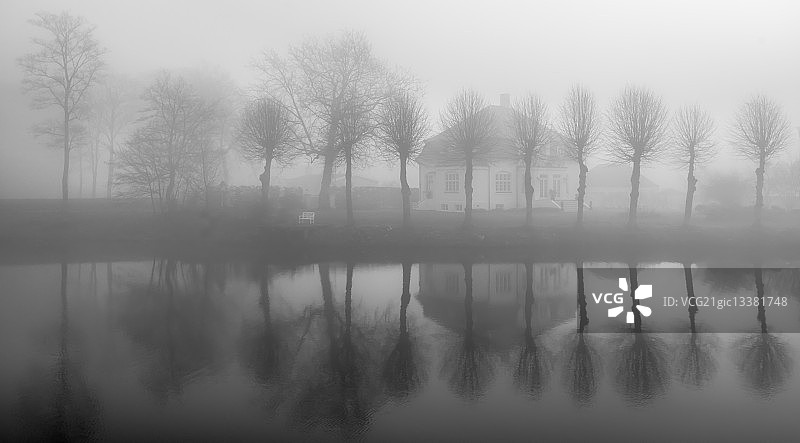 丹麦尼堡，福宁，雾中房子和树木的对称倒影图片素材