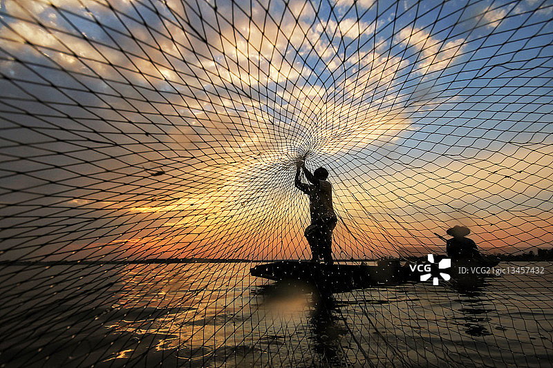 一个渔民抛出渔网的剪影。图片素材
