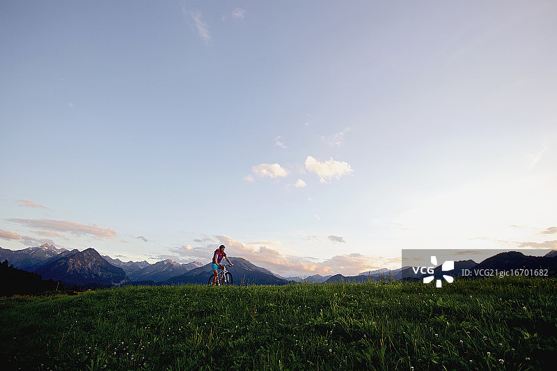 一个女人骑着她的自行车在阿尔卑斯山的全景前图片素材