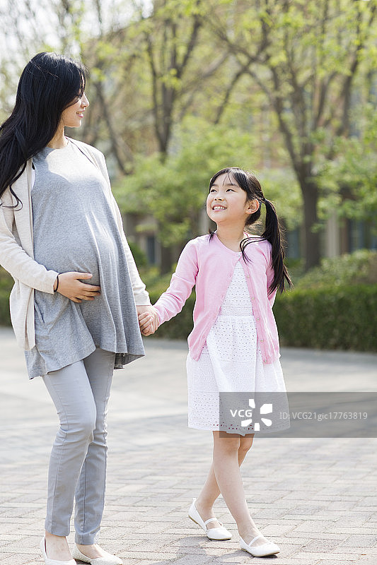 怀有身孕的妈妈和女儿手牵手散步图片素材