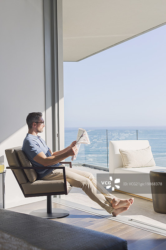 男人放松阅读报纸在阳光灿烂的露台门口与海景图片素材