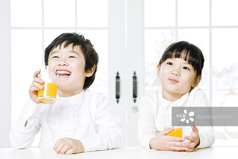 男孩和女孩坐在桌子上，喝着橙汁图片素材