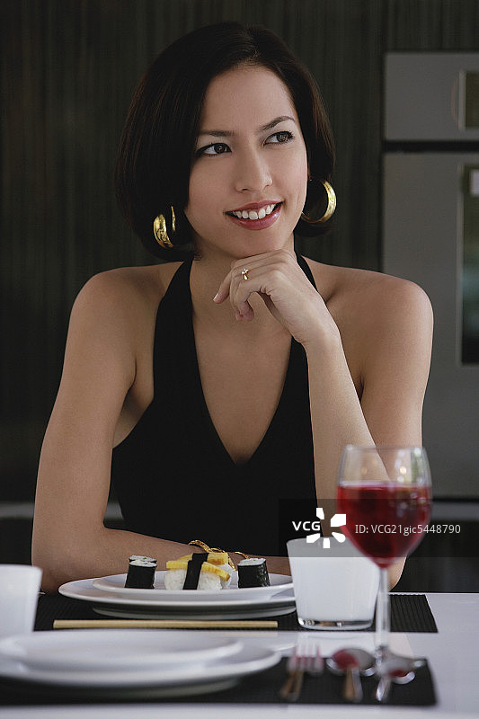 一位女士坐在桌子旁，桌上放着一盘寿司和一杯红酒图片素材