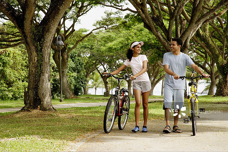 一对情侣在公园里散步，手里拿着自行车图片素材