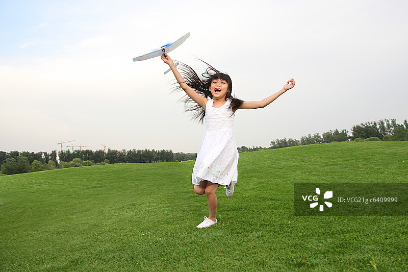 一个东方女孩在草上玩飞机模型图片素材