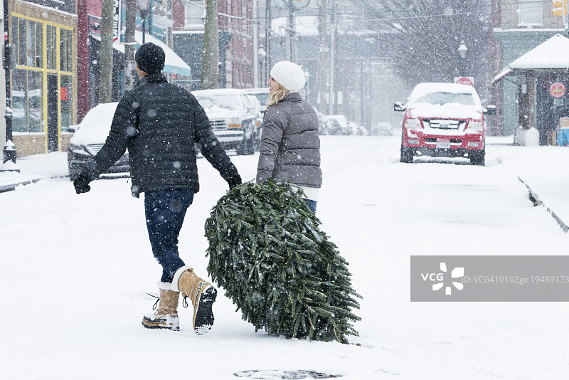 一对夫妇在雪中拖着圣诞树图片素材