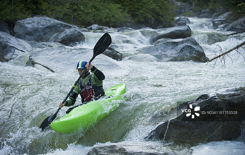 一名激流皮划艇运动员继续沿着一条高山河流的岩石段滑行。图片素材