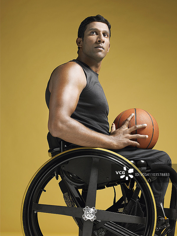 截瘫运动员坐在轮椅上抱着篮球，侧面图片素材
