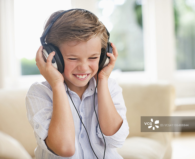 男孩(10-11岁)在家里通过耳机听音乐图片素材