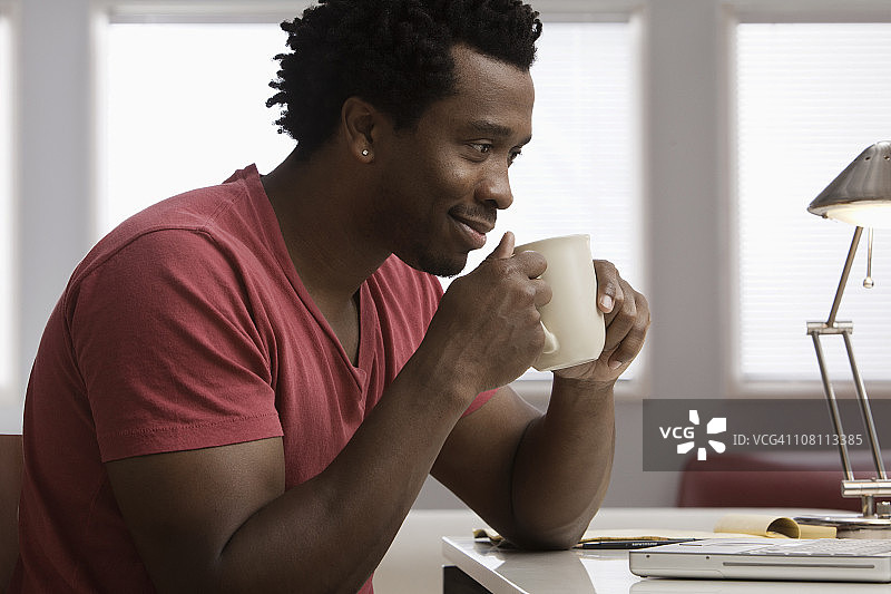 微笑的黑人在家庭办公室的桌子上喝咖啡图片素材