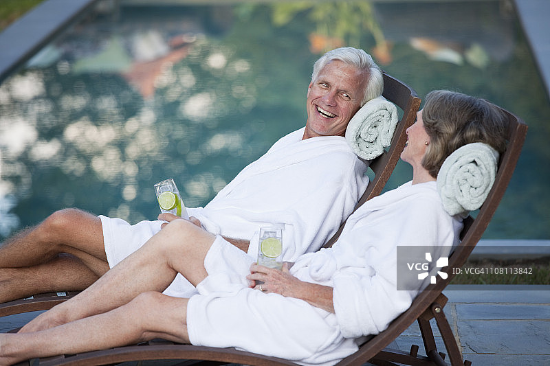 一对穿着长袍的夫妇在泳池边的躺椅上放松图片素材