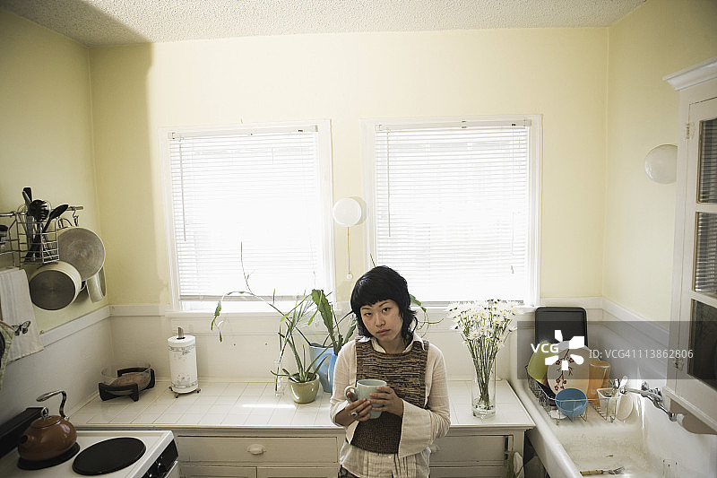 一个年轻女人站在厨房里拿着杯子图片素材