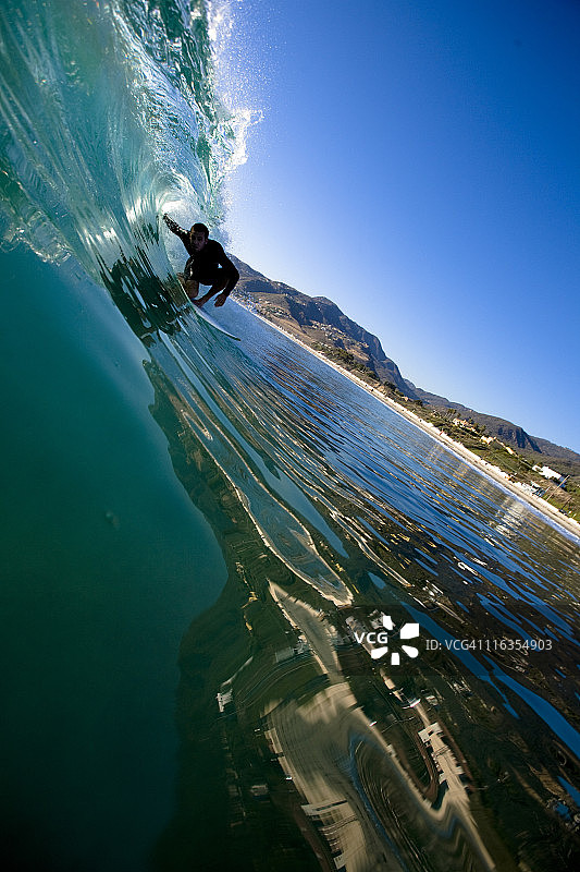 一名男性冲浪者在加州马里布的祖玛海滩冲浪时，正站在一个玻璃桶前。图片素材