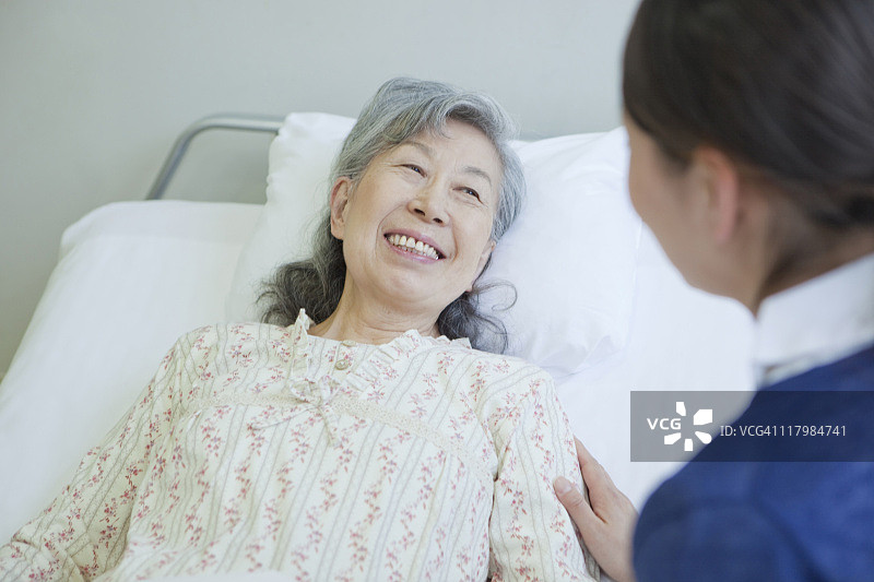 日本本州神奈川县，一位老年妇女躺在床上与护士交谈图片素材