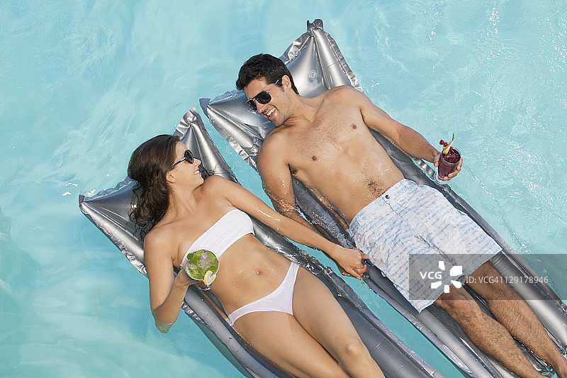 微笑的夫妇拿着杯子躺在木筏上图片素材