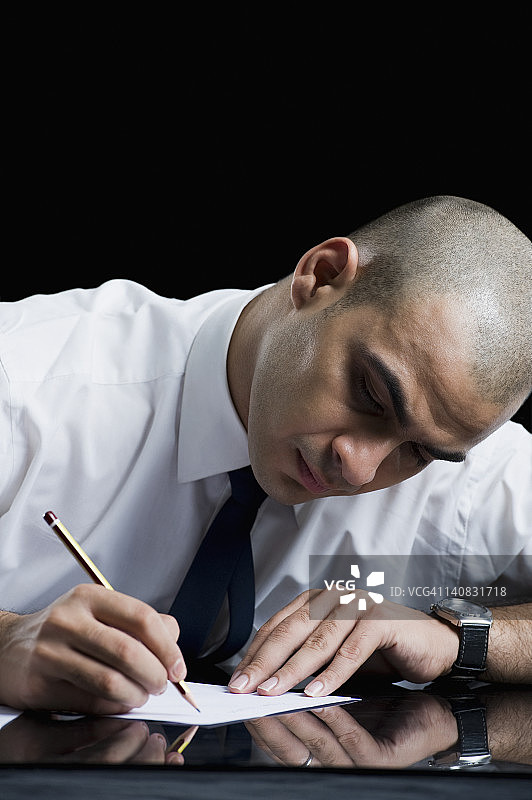 一个商人坐在桌子旁，在一张纸上写着图片素材