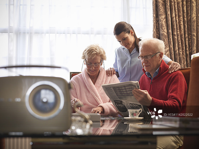 护士协助老年夫妇阅读报纸图片素材