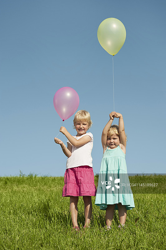 德国，巴伐利亚，女孩们拿着气球站在草地上图片素材