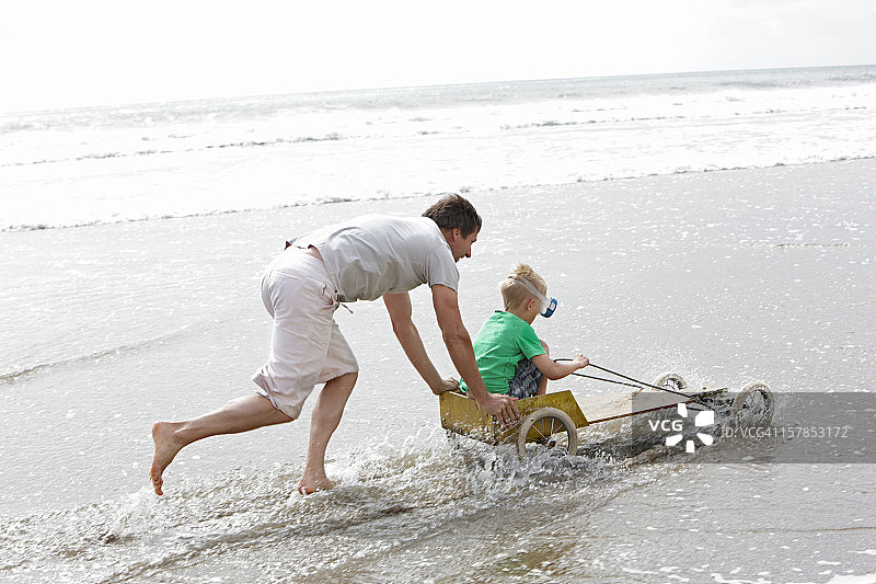 父亲在沙滩上推着儿子玩卡丁车图片素材