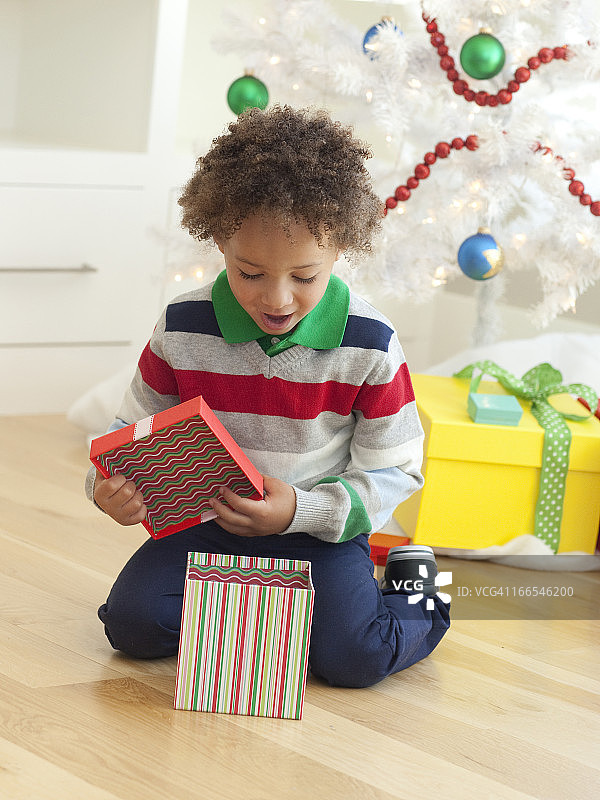 小男孩坐在圣诞树下，打开圣诞礼物图片素材