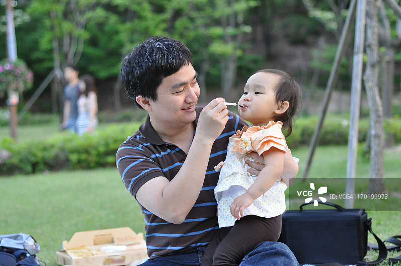 一个亚洲小孩和她爸爸在公园里吃饭图片素材