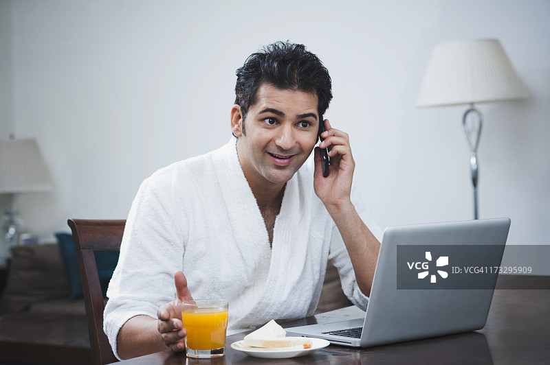 一个商人坐在笔记本电脑前，在早餐桌上用手机聊天图片素材