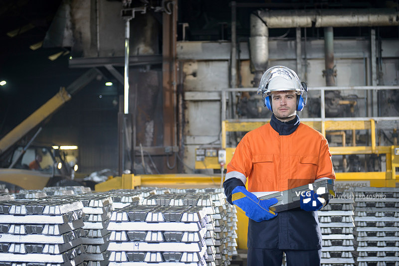 在铸造厂，工人穿着防护服搬运铝锭图片素材