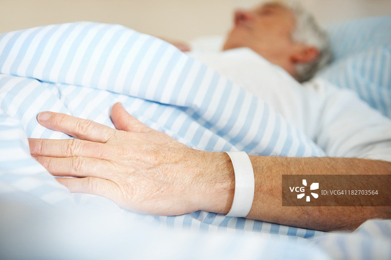 一名男子躺在医院病床上，手上拿着一条绷带图片素材