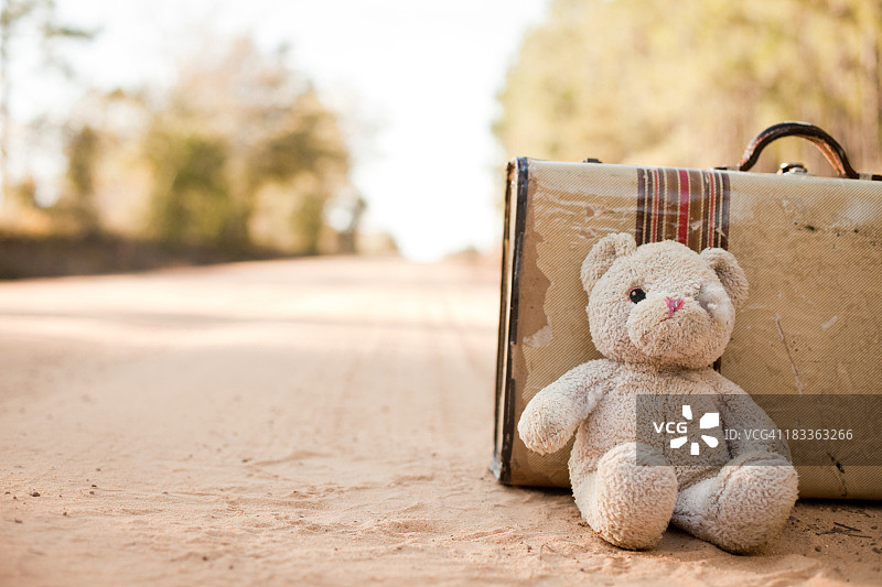 被遗弃的手提箱和泰迪熊在土路上图片素材